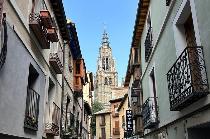 A narrow street of balconied houses in Toledo with the Cathedral spire closing the view